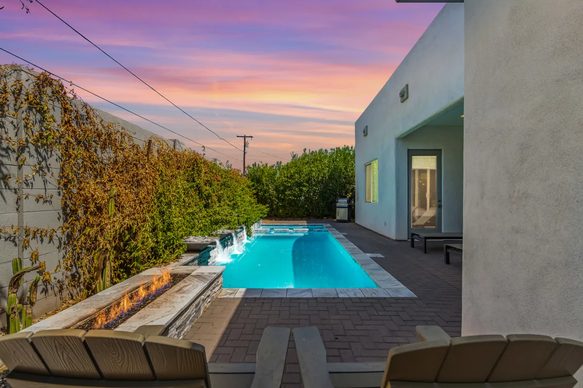 A modern backyard poolscape featuring a sleek swimming pool, a built-in fire feature, and surrounding greenery. The pool area is set against contemporary architecture, and the fire feature promises cozy evenings under the stars.