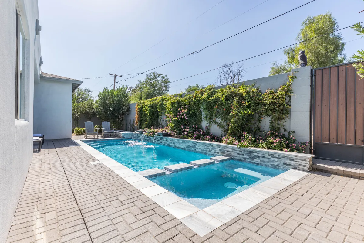 A tranquil pool area highlighted by a stone fountain and lush green landscaping, with ample outdoor seating nearby. The area is bathed in natural light, suggesting morning coffee or afternoon relaxation, and the seating arrangement hints at potential for group gatherings.