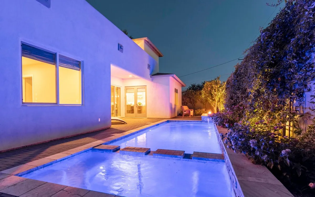 The hero image showcases a sparkling swimming pool glowing under ambient evening lights, with inviting illuminated windows and lush desert landscaping surrounding the area. The tranquil setting suggests opportunities for nighttime swims, outdoor gatherings, and relaxing conversations beside the water.