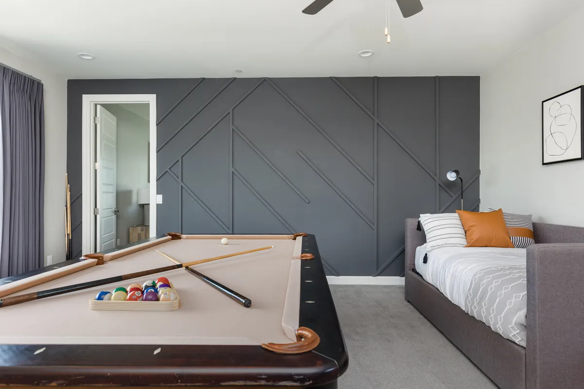 An inviting entertainment lounge with a modern pool table as the focal point, complemented by a textured accent wall and a cozy sofa with cushions. The setup is perfect for game nights and relaxed socializing.