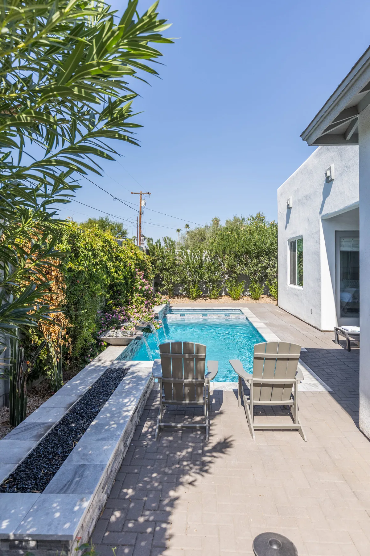 A serene outdoor space featuring a sparkling swimming pool surrounded by lush landscaped gardens and a row of comfortable lounge chairs. The scene exudes a tranquil and inviting vibe, ideal for relaxation or socializing under the desert sun.