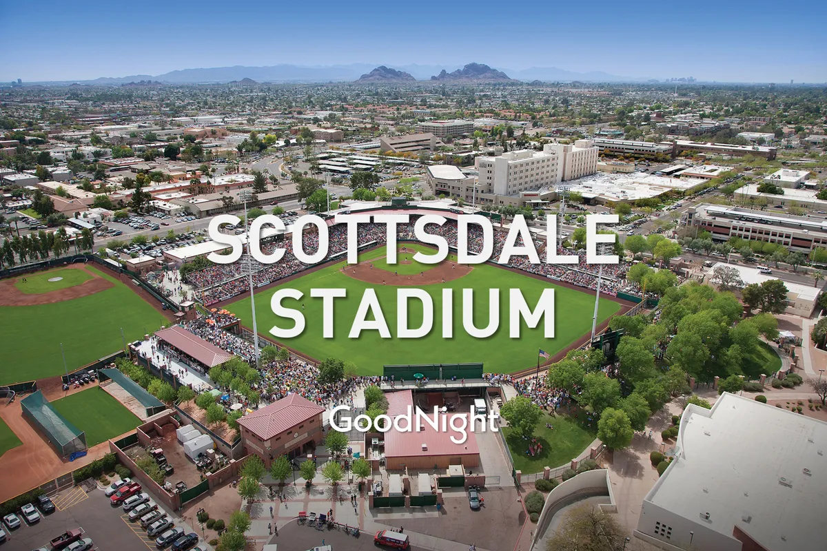 An energetic exterior scene captures a baseball field bustling with spectators, set against a cityscape and mountainous backdrop. The festive mood hints at community events and special outings.