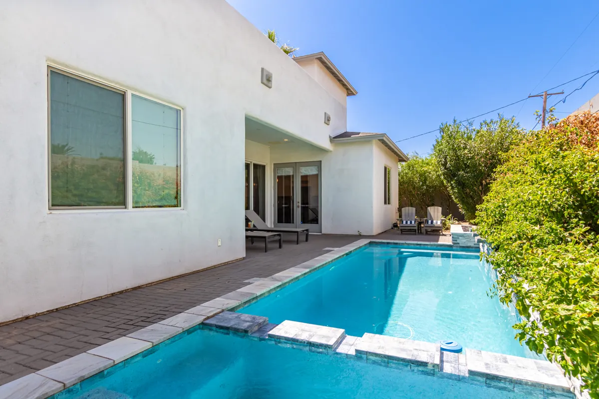 A relaxed outdoor patio and pool area, blending swimming, sunbathing, and outdoor dining opportunities amidst surrounding greenery. Lounge chairs and a spacious patio invite guests to enjoy both daytime and evening gatherings.