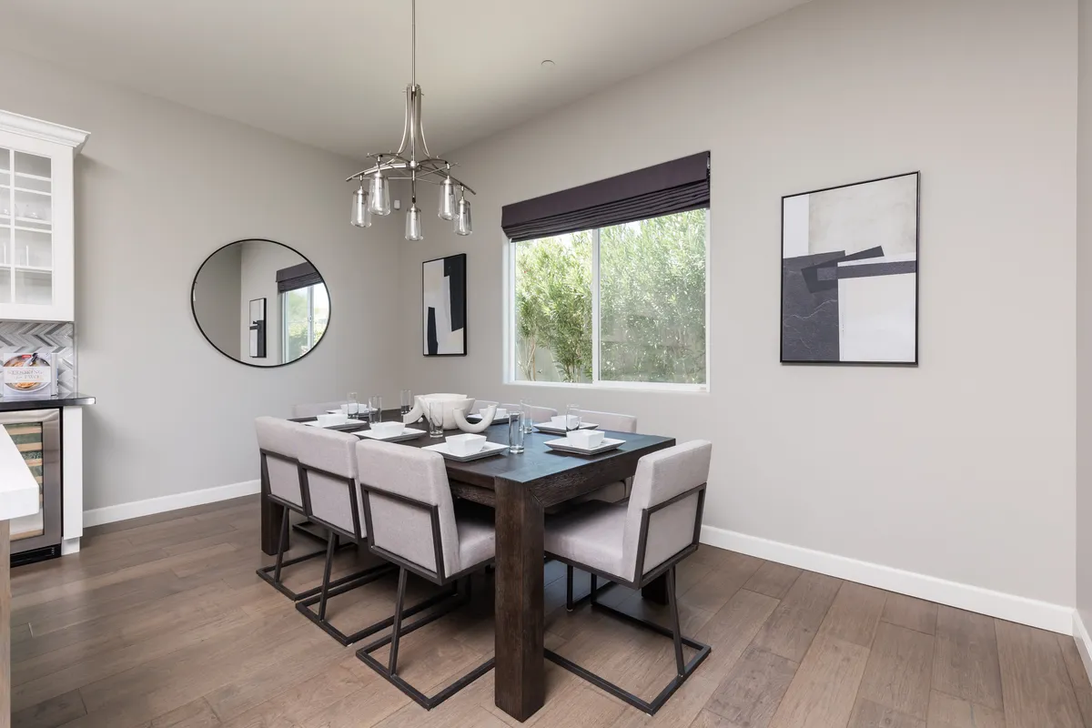 A contemporary dining area with a long table set for twelve, a striking chandelier overhead, and artwork adorning the walls. A large window provides extra light, making the space ideal for shared meals and celebrations.