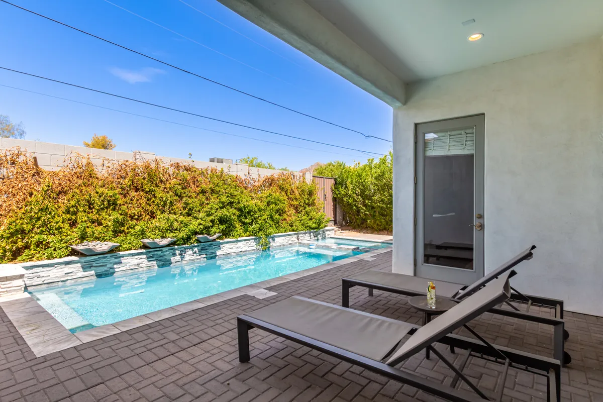 A tranquil poolside setting with lounge chairs arranged around a bright blue swimming pool and a well-manicured hedge, offering both privacy and luxury. The scene suggests an environment made for sunbathing, casual gatherings, and unwinding outdoors.