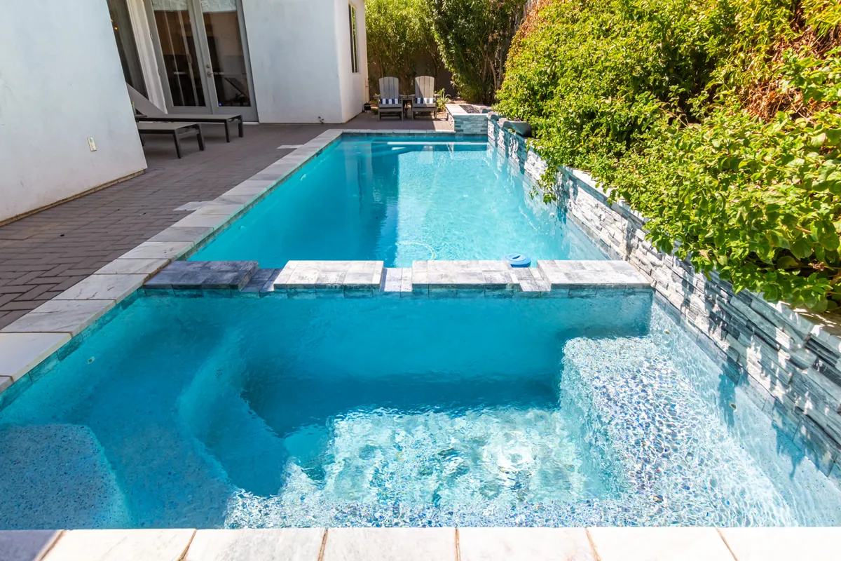 This image features an exterior view of a vibrant swimming pool surrounded by lounge chairs and lush greenery. The tranquil setting is highlighted by natural sunlight, inviting guests to enjoy relaxing swims or poolside gatherings.